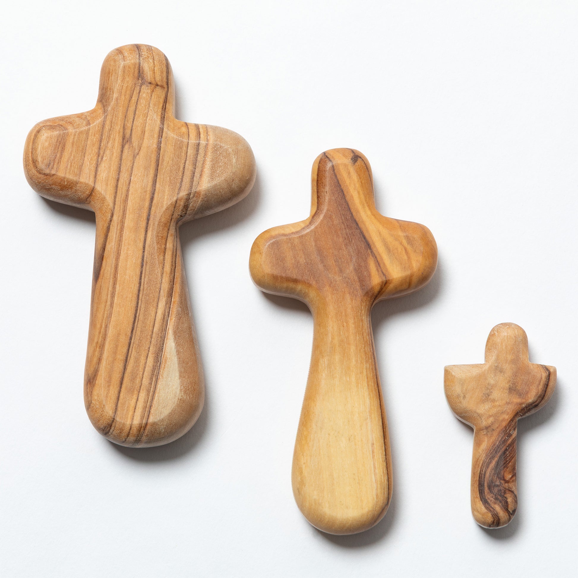 Three olive wood crosses in different sizes arranged diagonally on a clean white background.