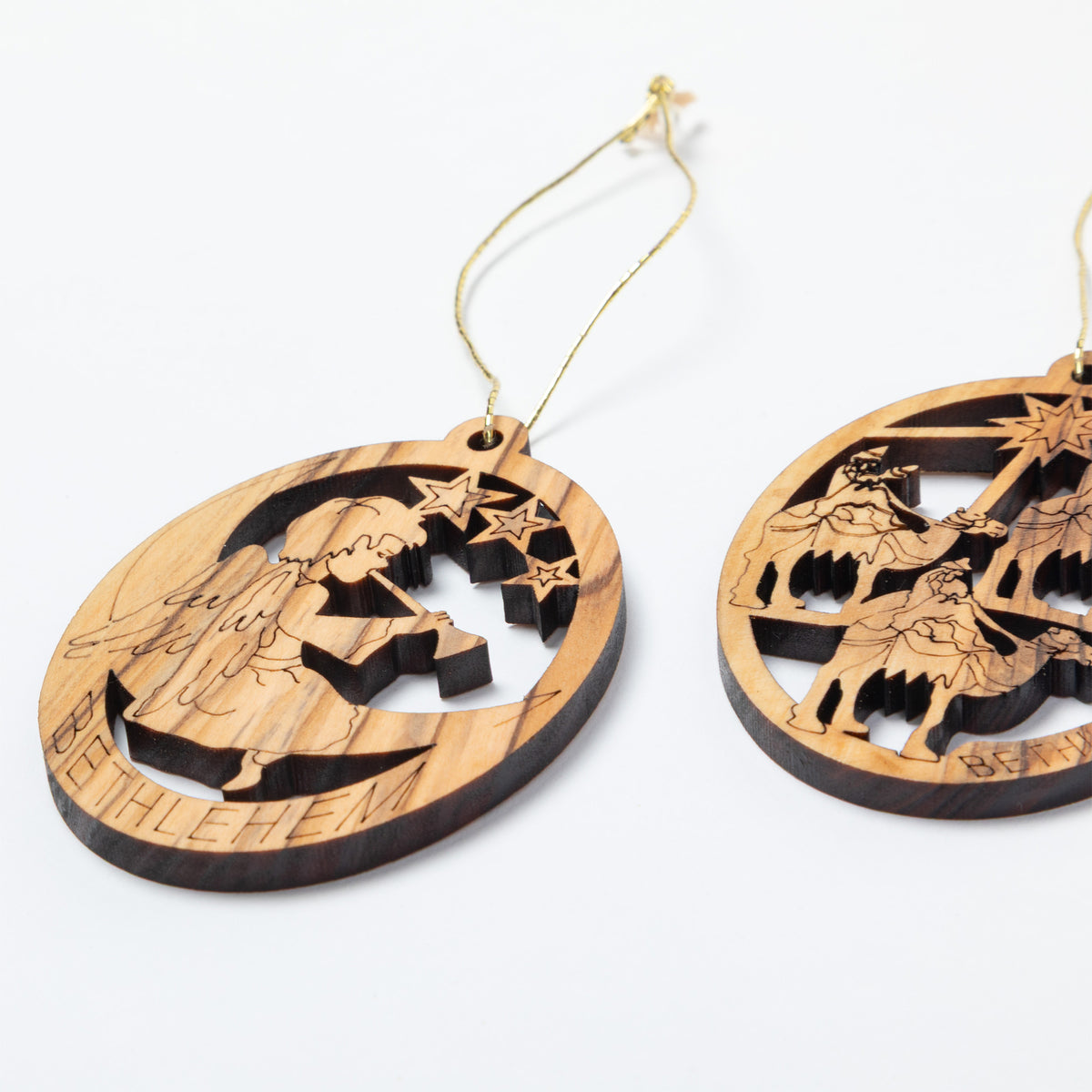 Two oval wooden Christmas ornaments with hanging loops, featuring laser-cut nativity and Bethlehem scenes on a light wood background with darker burned edges, shown on a white background.