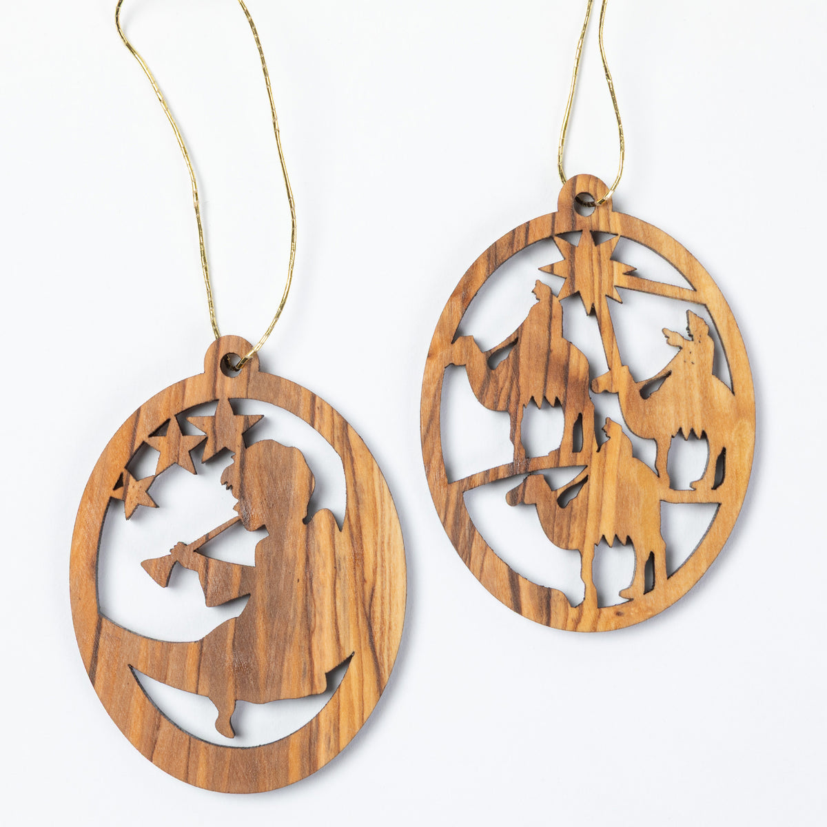 Two oval wooden Christmas ornaments with laser-cut nativity scenes, hanging from light tan strings against a plain white background.