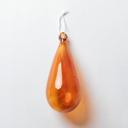 An amber teardrop-shaped glass ornament with a white hanging string, shown against a plain white background.