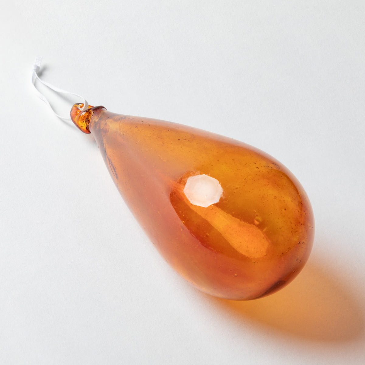 An amber glass teardrop-shaped hanging ornament with a white hanging string, photographed on a clean white background.