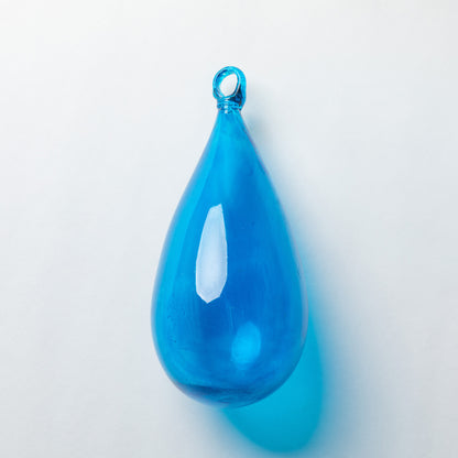 A glossy, teardrop-shaped blue glass pendant with a small hanging loop at the top, shown on a clean white background with a soft blue shadow.