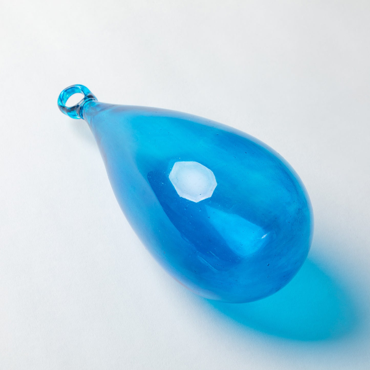 A translucent blue glass teardrop pendant with a small loop at the top, photographed on a clean white background with a soft shadow.