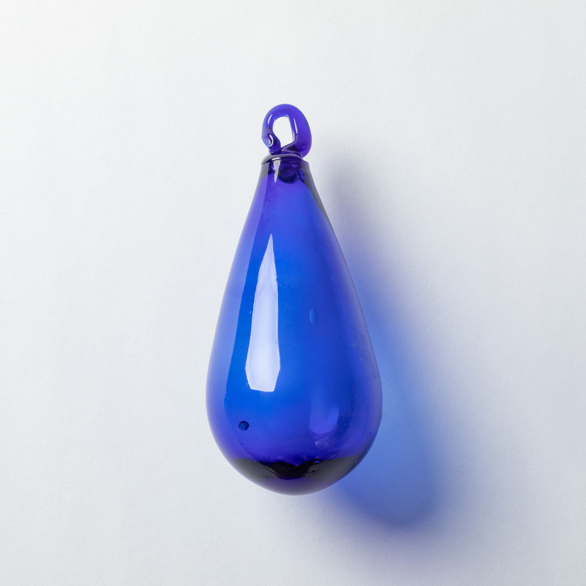 A glossy cobalt blue glass teardrop pendant with a small loop at the top, shown against a plain light gray background.