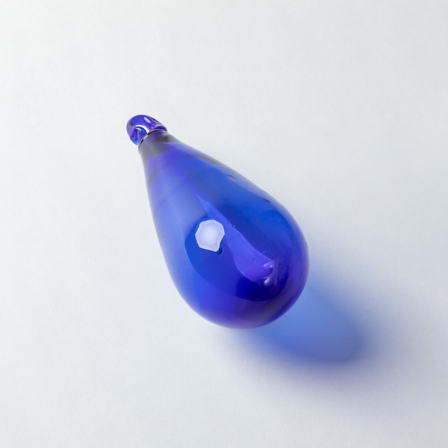 A teardrop-shaped cobalt blue glass pendant with a textured, ribbed surface and a small loop at the top, shown on a light gray background with a soft shadow.