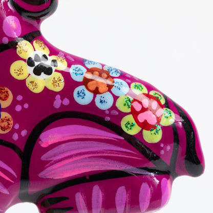 Close-up of a glossy pink dog magnet with hand-painted floral patterns in yellow, blue, red, green, and orange, along with black outlines and a black paw print detail on the back.