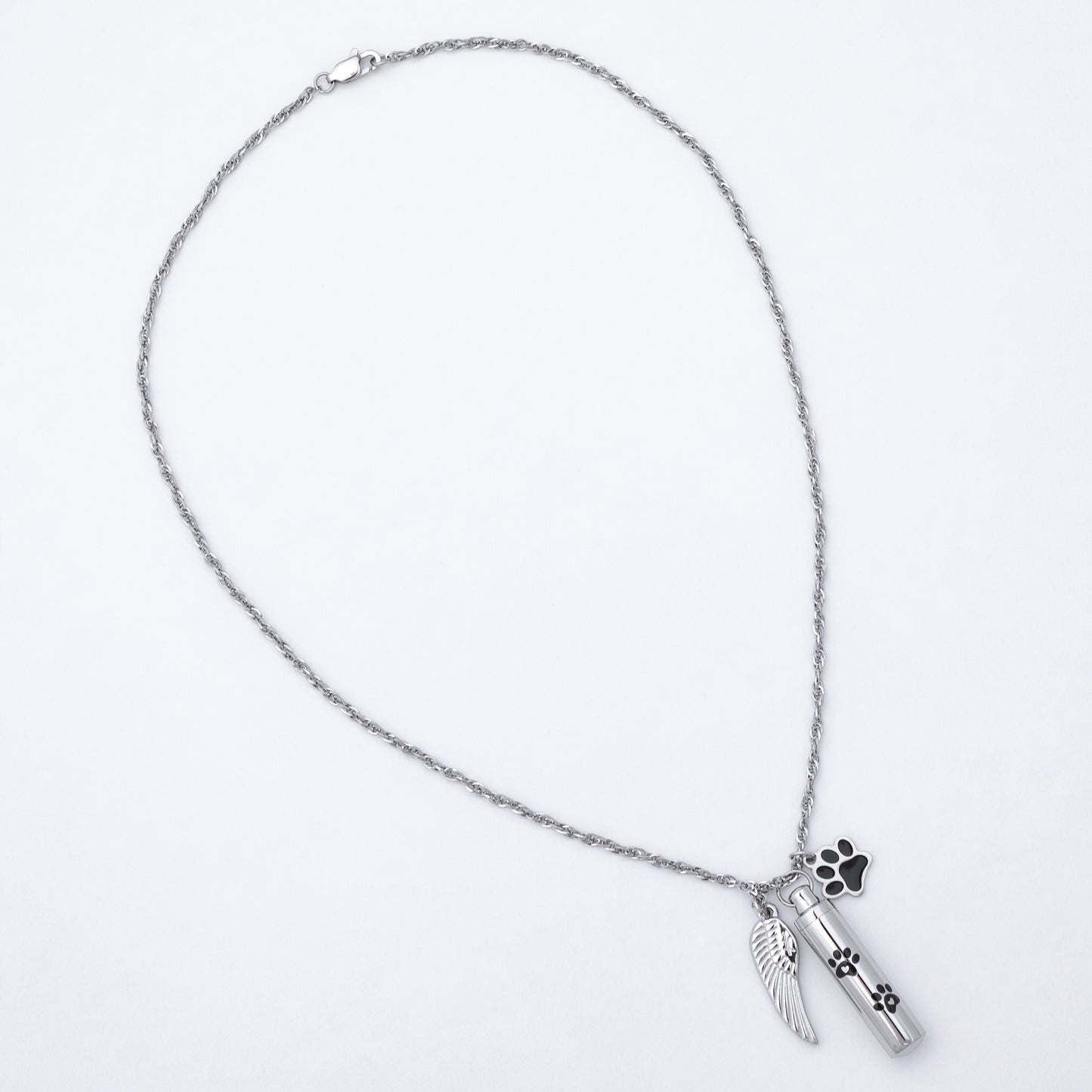 A silver-toned chain necklace featuring a cylinder urn pendant with a small wing charm and a paw print charm, displayed on a clean white background.