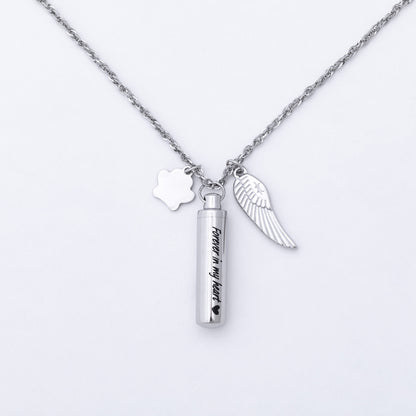 A silver chain necklace featuring three charms: a paw print, a wing, and a cylindrical urn pendant engraved with 'Forever in my heart'.