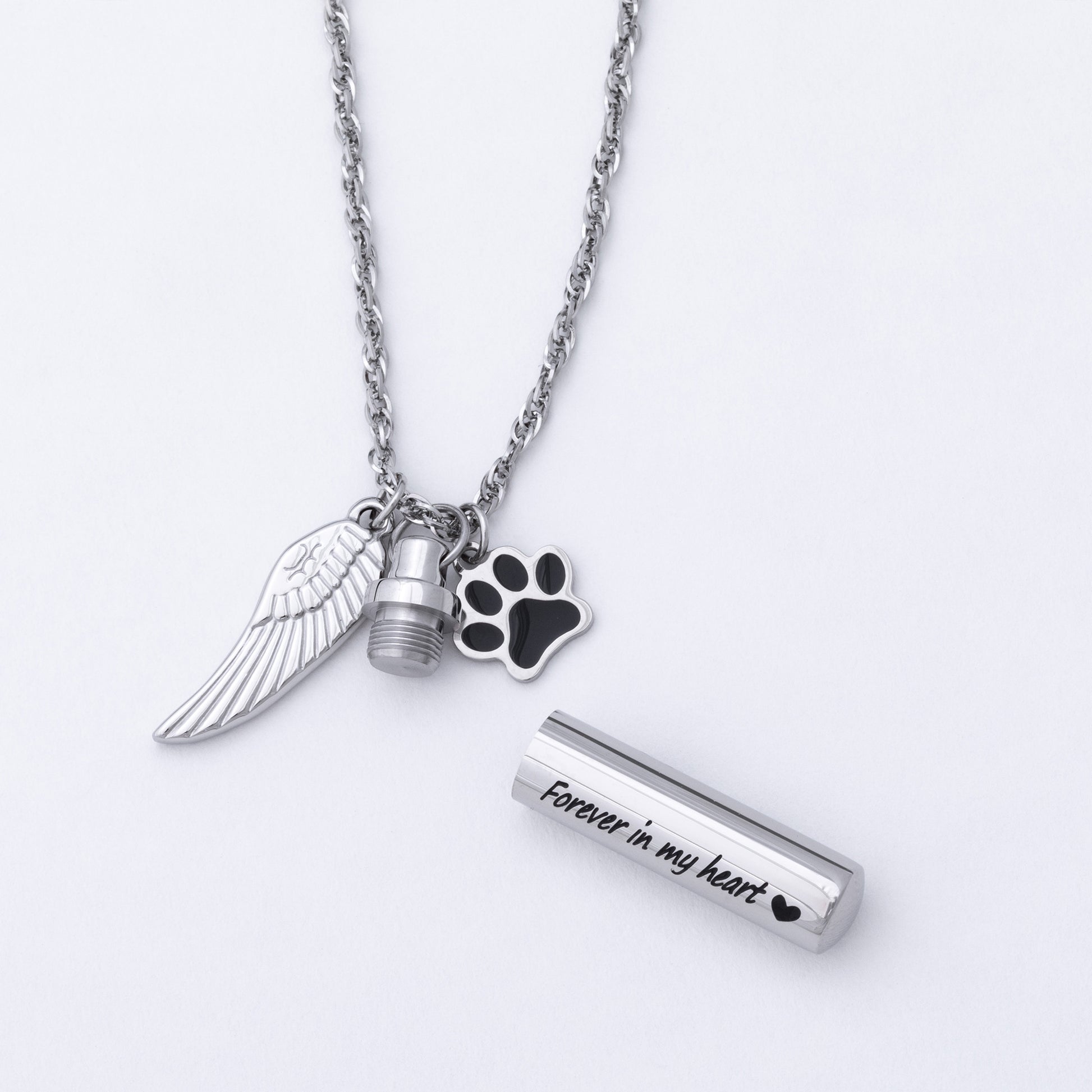Silver-tone memorial necklace with a wing charm, a paw print charm, a small urn charm, and a cylindrical keepsake tube engraved with 'Forever in my heart' on a white background.