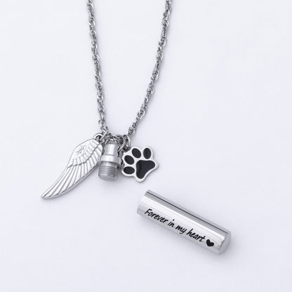 Silver-tone memorial necklace with a wing charm, a paw print charm, a small urn charm, and a cylindrical keepsake tube engraved with 'Forever in my heart' on a white background.