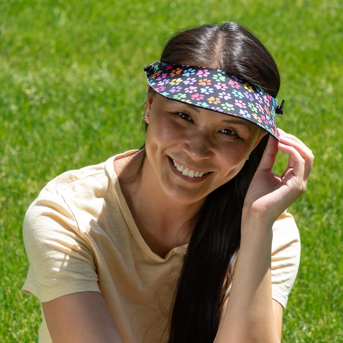 Woman wearing a colorful paw print visor against a green grass background