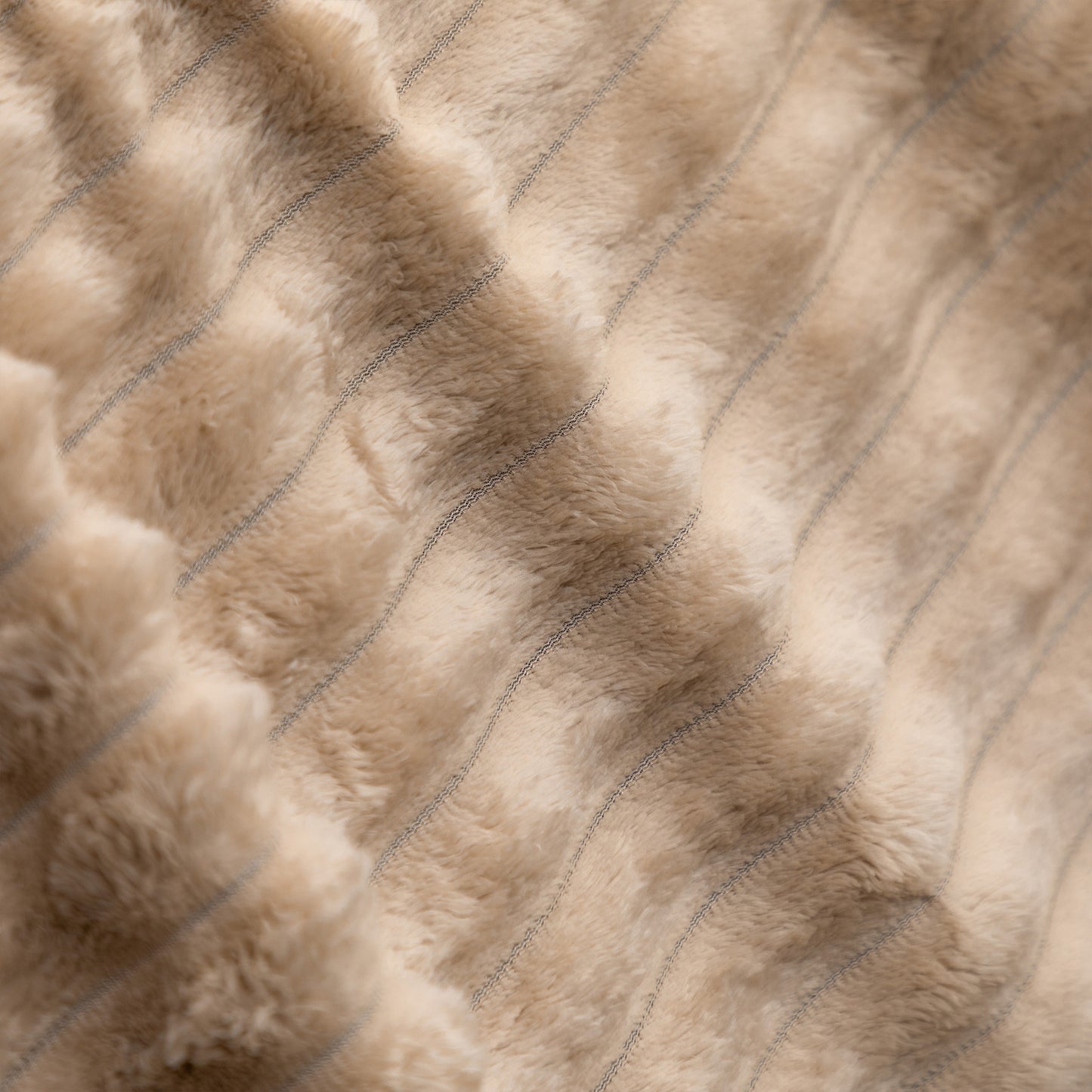 Close-up of a plush faux fur or sheepskin-style textile in a warm beige/taupe tone with subtle stitched vertical channeling.