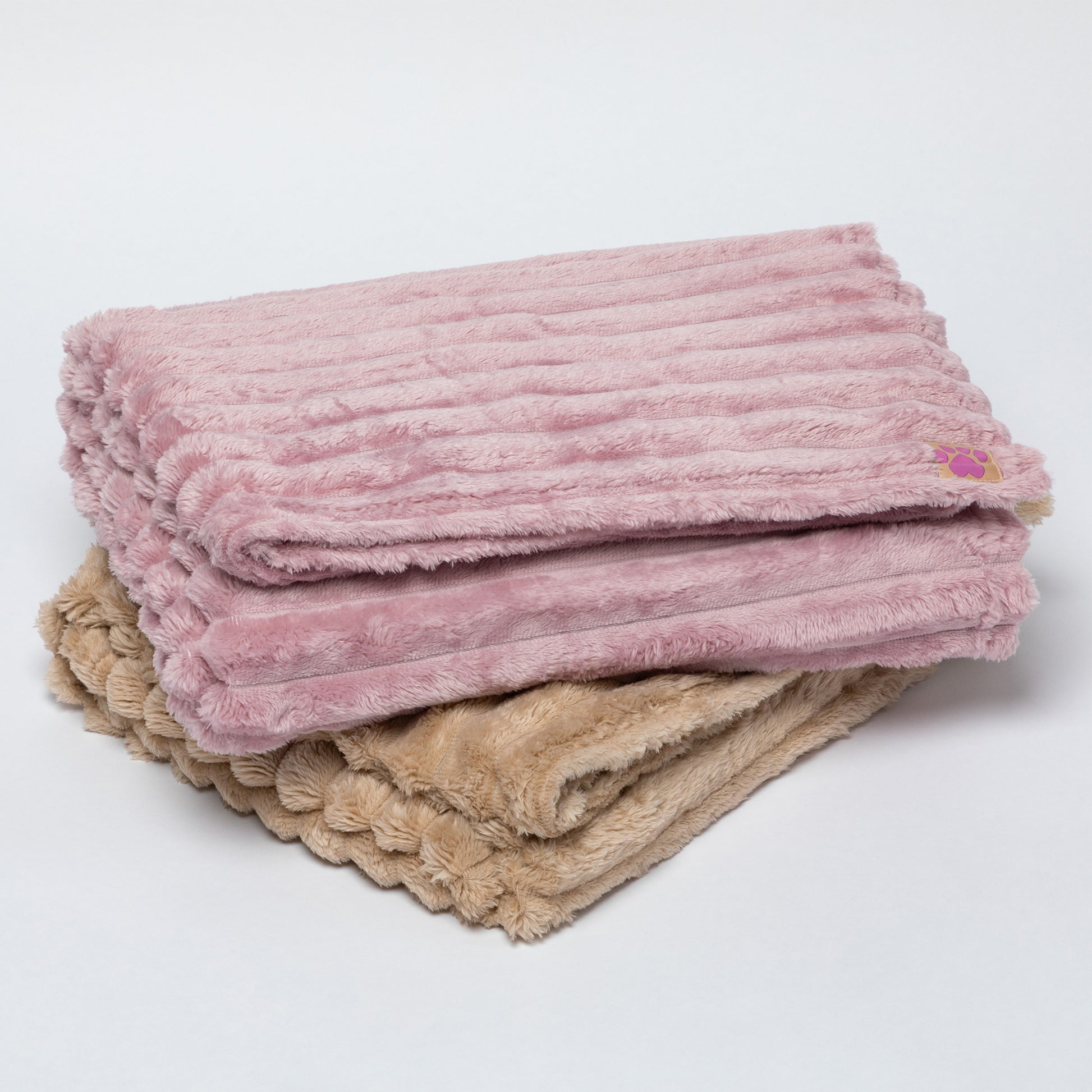 Two folded plush ribbed blankets stacked on a light gray background. The top blanket is dusty pink, and the bottom blanket is beige with a scalloped edge.