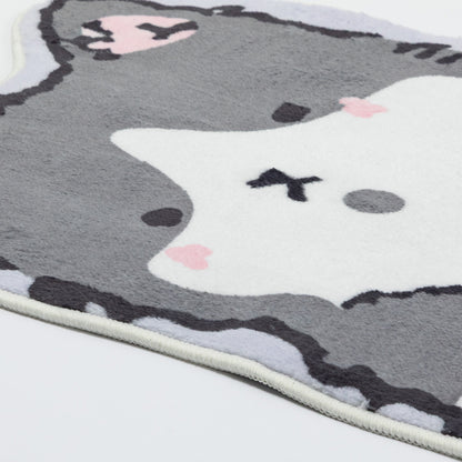 A close-up of a plush gray and white cat-shaped rug with pink heart-shaped cheeks and black facial details, shown on a white background.