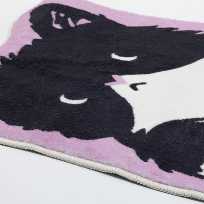 A close-up of a plush blanket featuring a stylized black cat face on a light pink background, with a white stitched edge visible along the bottom.