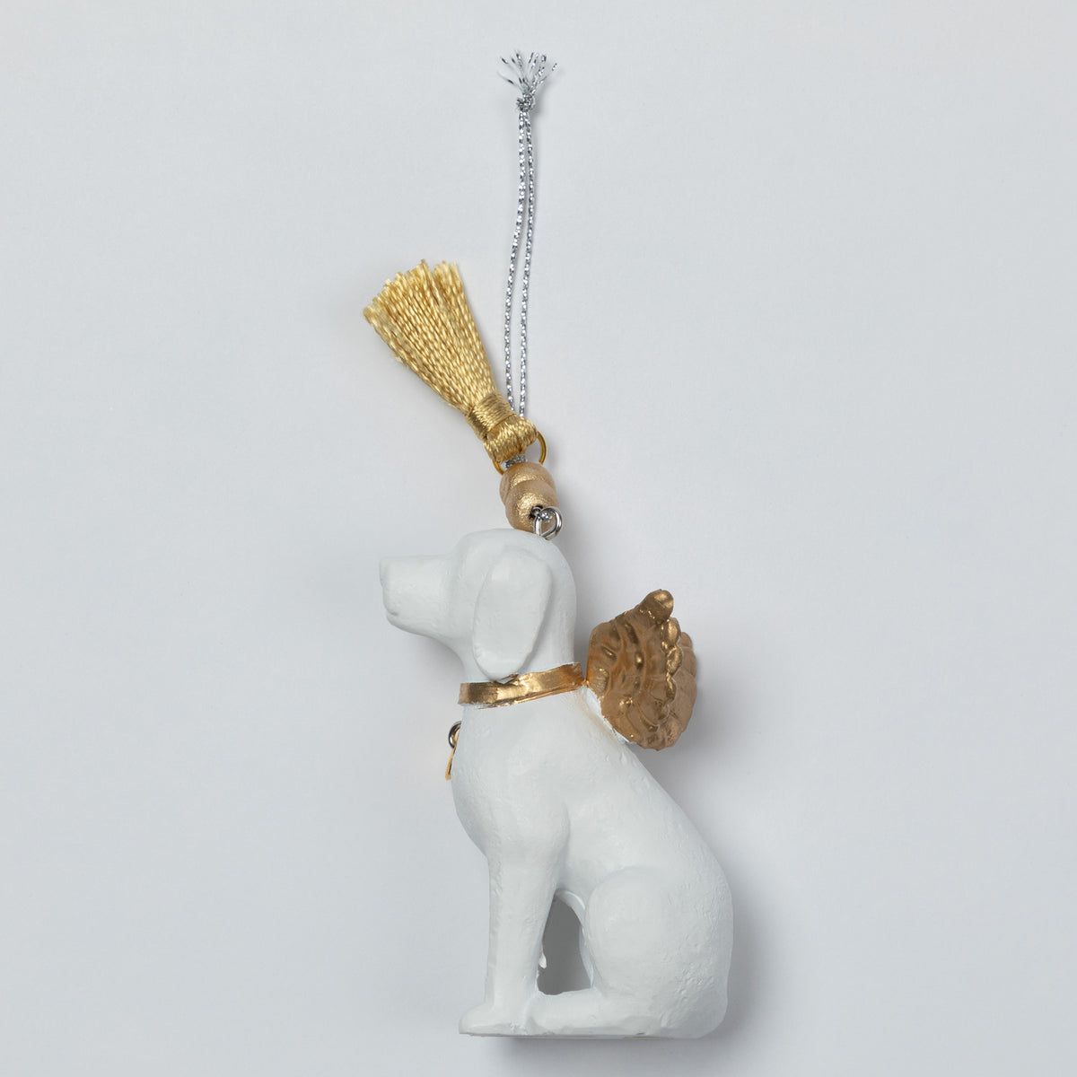 A white angel dog ornament with gold wings, collar, and tassel, hanging from a silver chain against a light gray background.