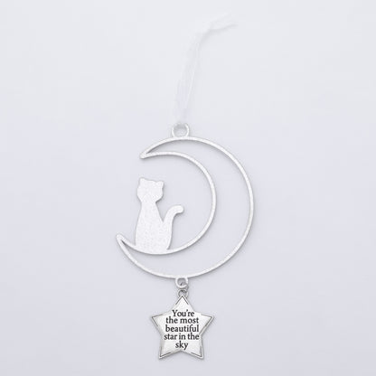 A silver-toned metal hanging ornament featuring a crescent moon silhouette with a seated cat cutout and a dangling star charm that reads, 'You're the most beautiful star in the sky.'.
