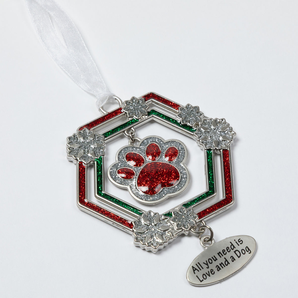 A silver-toned Christmas ornament featuring a red glitter paw print in the center, surrounded by a hexagonal frame with red and green glitter stripes and clear rhinestone snowflake accents. A dangling silver tag reads 'All you need is Love and a Dog' and hangs from a white ribbon on a white background.