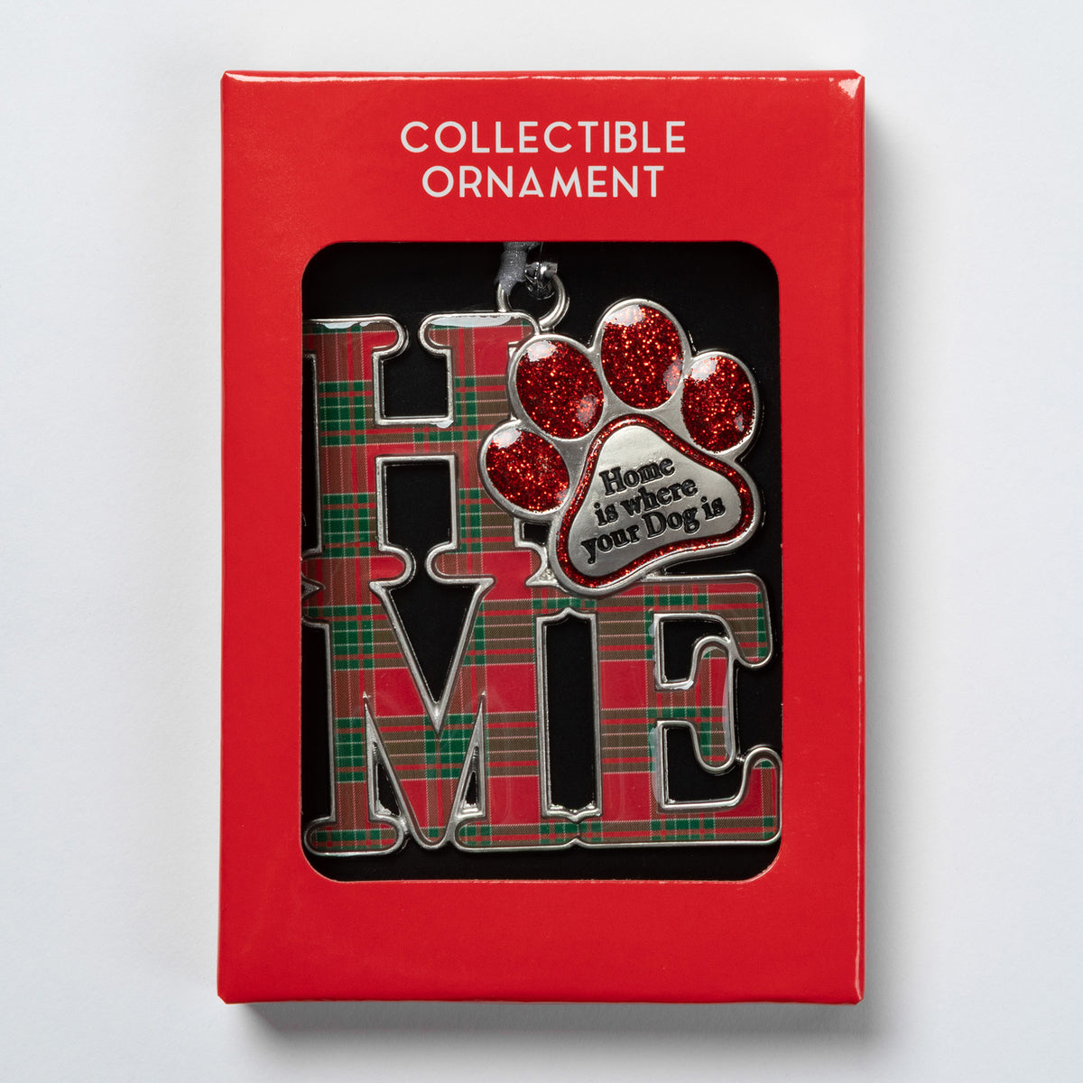 A collectible Christmas ornament displayed inside its red retail packaging. The ornament features the word 'HOME' in large silver letters with a red and green plaid pattern, alongside a red glitter paw print and a silver heart-shaped tag that reads 'Home is where your Dog is'.