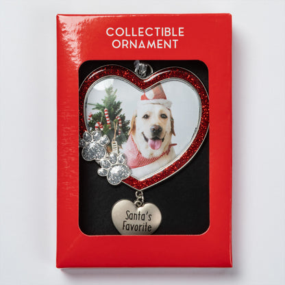 A red collectible ornament package with a heart-shaped window displaying a custom photo ornament. The ornament features a red glitter heart border, a silver paw print charm, and a dangling silver heart tag engraved with 'Santa's Favorite'.