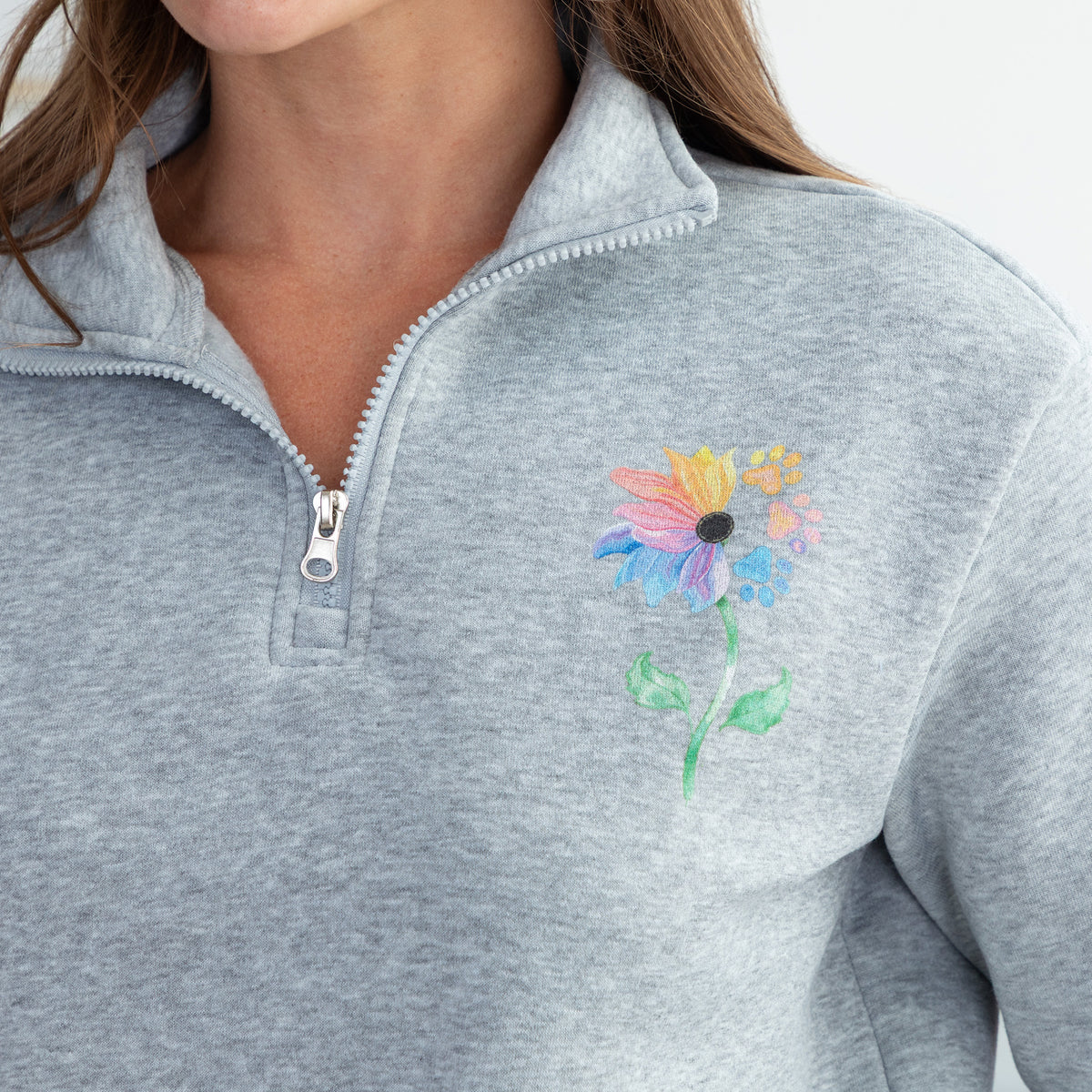 Close-up of a person wearing a heather gray quarter-zip pullover with a colorful flower on the left chest.