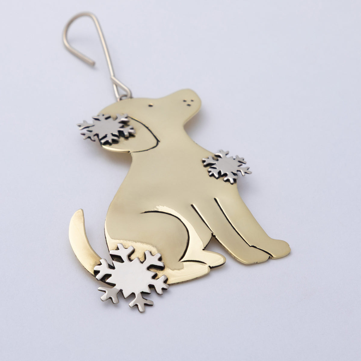 A polished gold-toned metal dog-shaped ornament with silver-toned snowflake accents on its chest and tail base, hanging against a plain light background.