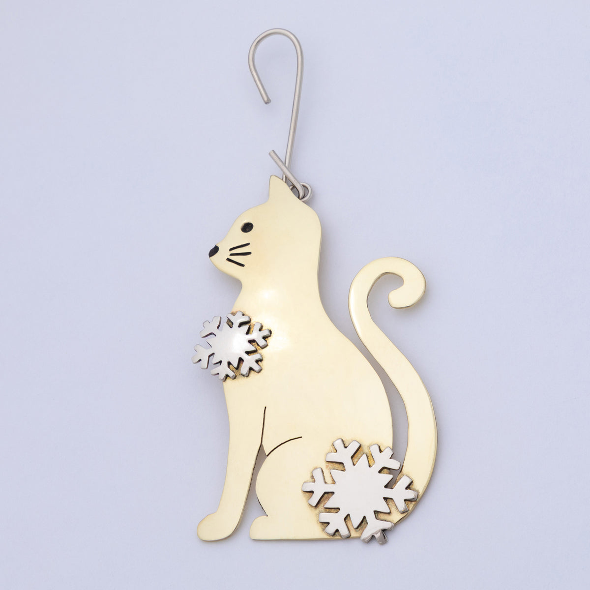 A polished gold-toned metal cat-shaped ornament with silver-toned snowflake accents on its chest and tail base, hanging against a plain light background.