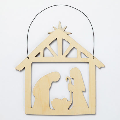 A light natural wood hanging nativity scene ornament with a black wire hanger, featuring silhouettes of Mary, Joseph, and baby Jesus under a star on a plain white background.