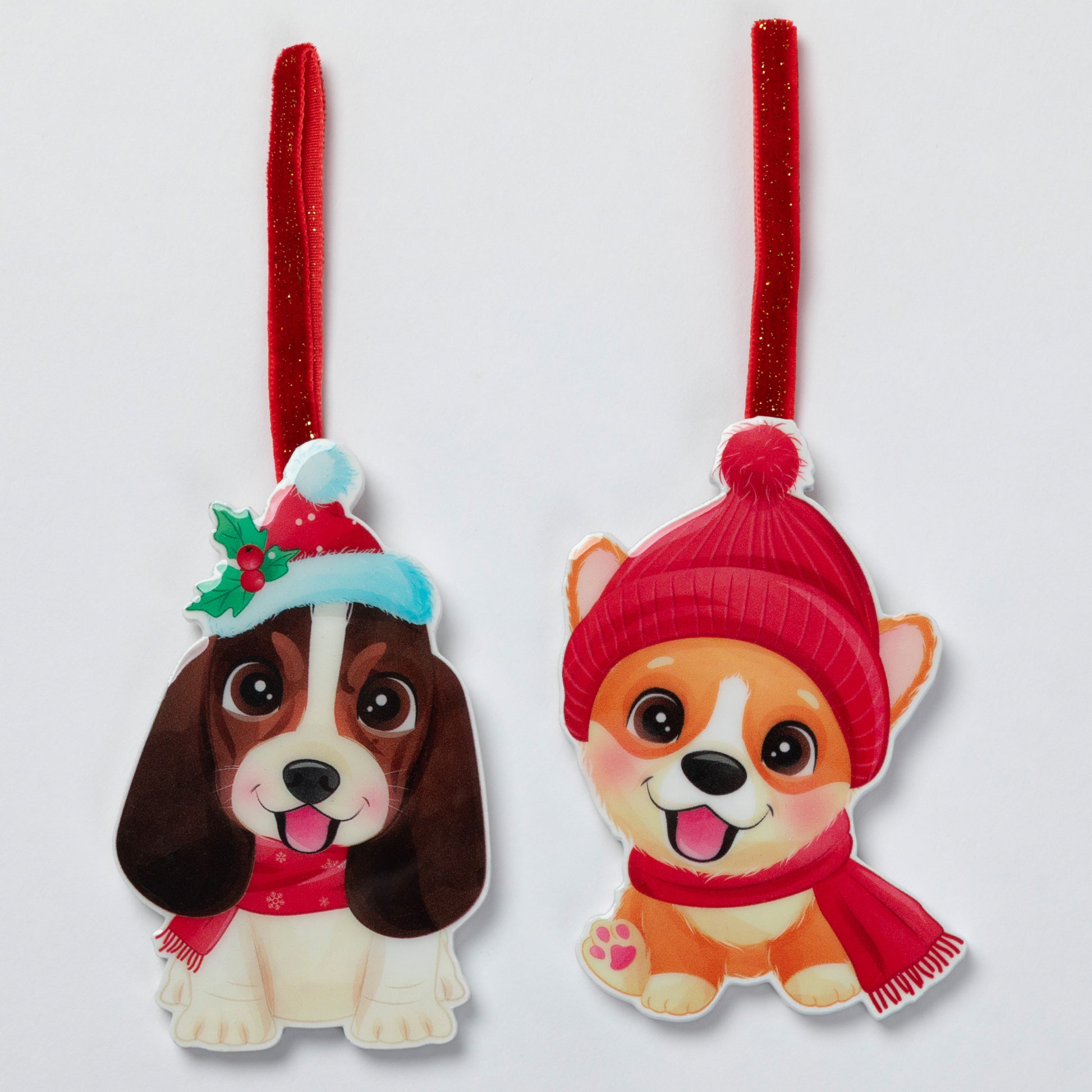Two Christmas hanging ornaments shaped like cartoon dogs, each with a red ribbon loop. One ornament shows a brown-and-white dog wearing a red Santa hat with green holly and a red scarf.