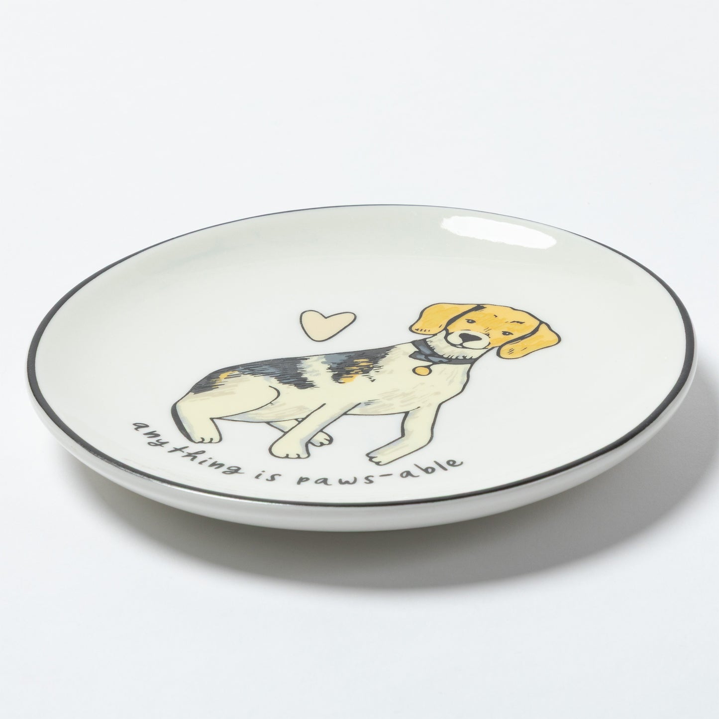 A white ceramic plate with a black rim, featuring a cartoon illustration of a beagle puppy with the text 'anything is paws-able' and a small heart on a white background.