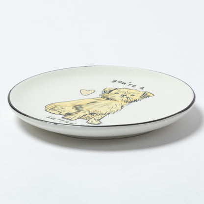A white ceramic plate with a black rim, featuring a hand-drawn illustration of a yellow dog with the text 'you're a' above it and 'in love' below it, shown on a clean white background.