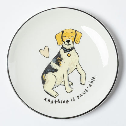 A round white ceramic plate with a black rim, featuring a hand-drawn illustration of a beagle puppy with the text 'anything is paws able' and a small heart.