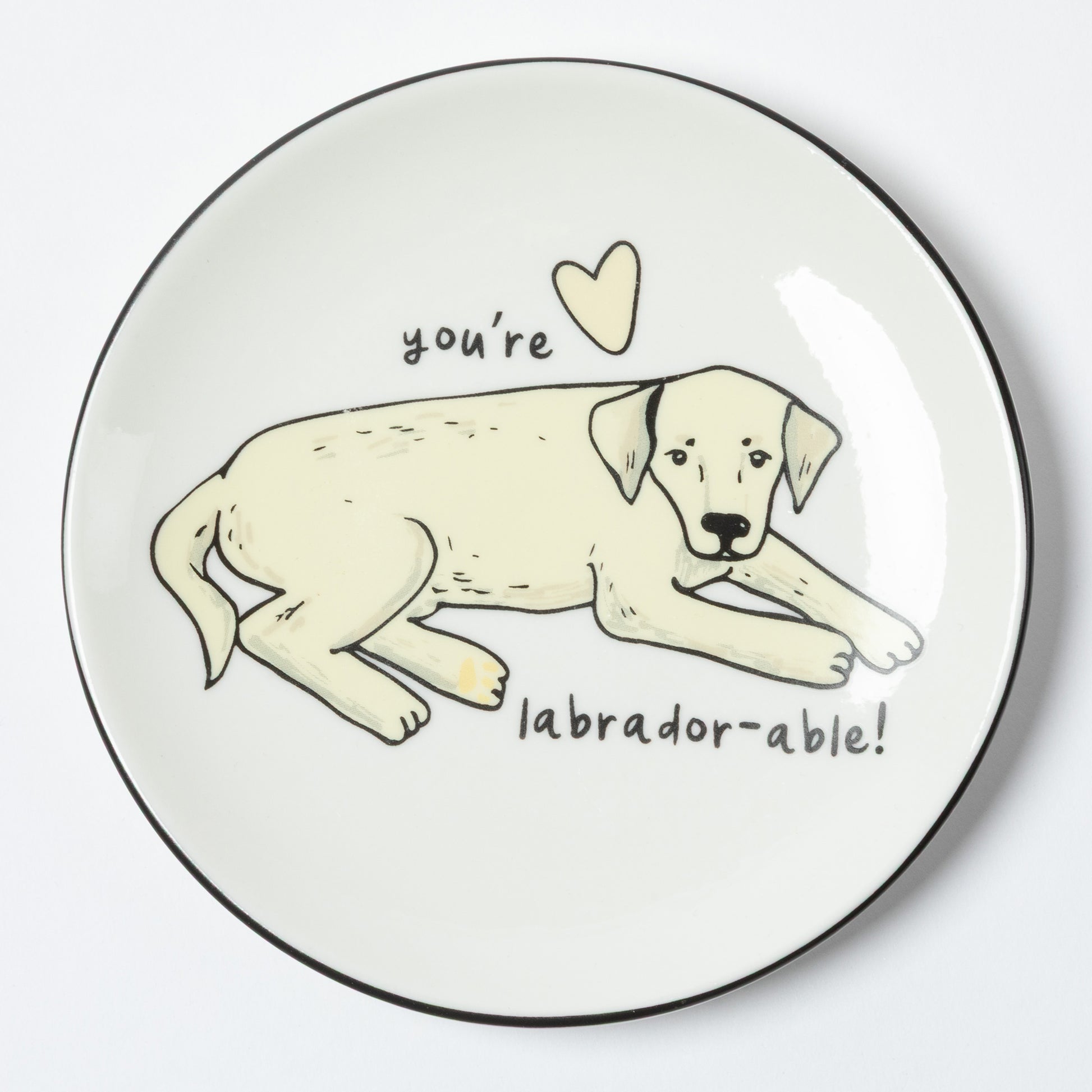 A round white plate with a black rim, featuring a hand-drawn illustration of a light cream Labrador puppy lying down with the text 'you're labrador-able!' and a small heart above it.
