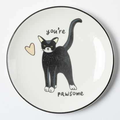 A round white plate with a black rim, featuring a black and white cat illustration with the words 'you're pawsome' and a small beige heart on a white background.
