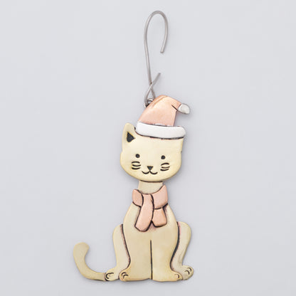 A whimsical cat-shaped ornament with brass body, a copper Santa hat, and matching scarf, hanging from a silver metal hook against a light gray background.