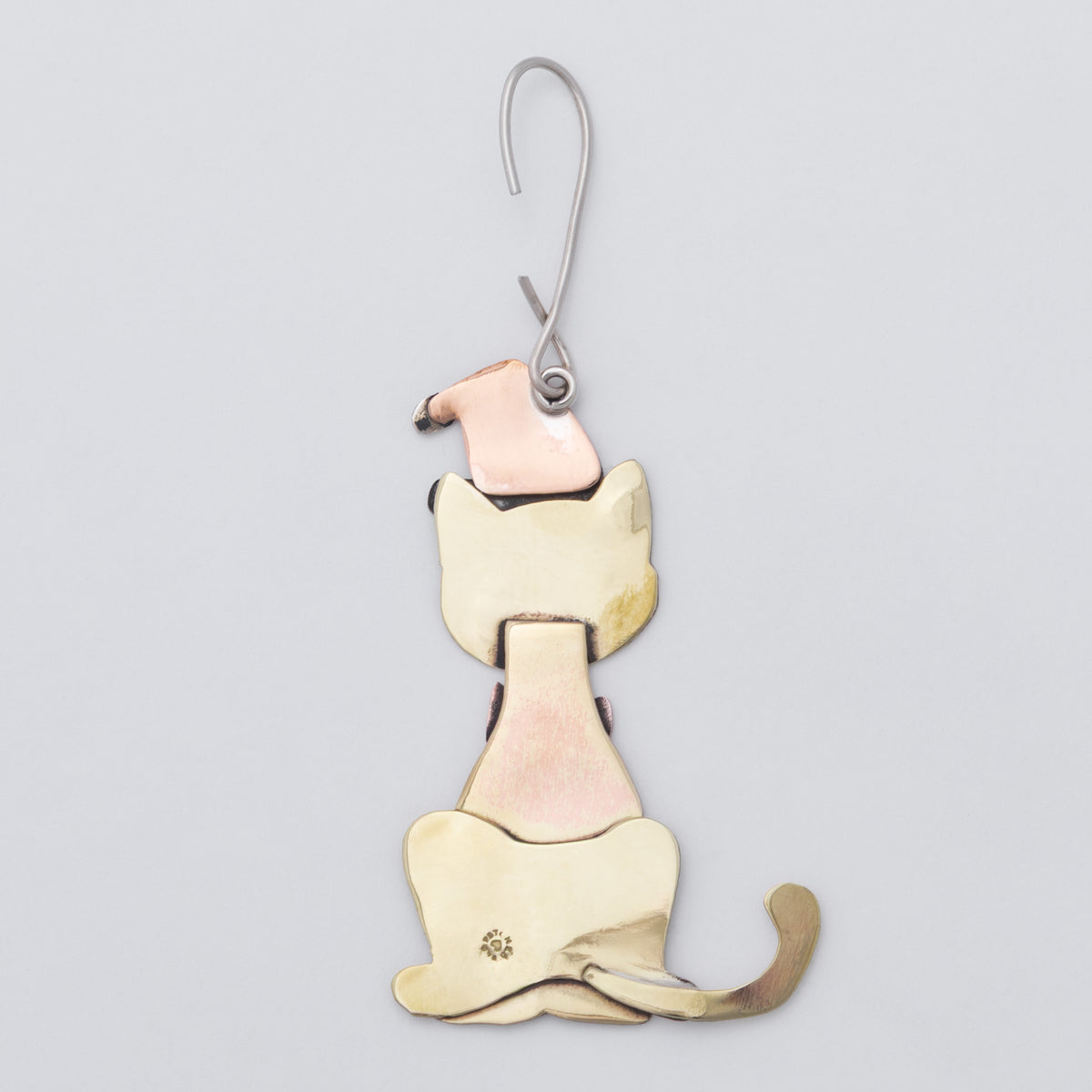 A whimsical cat-shaped ornament with brass body, a copper Santa hat, and matching scarf, hanging from a silver metal hook against a light gray background.