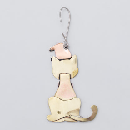 A whimsical cat-shaped ornament with brass body, a copper Santa hat, and matching scarf, hanging from a silver metal hook against a light gray background.