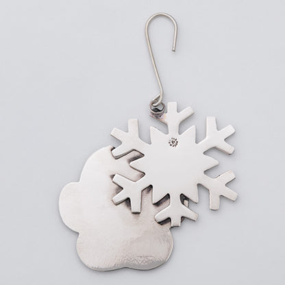 A metal snowflake and paw print ornament attached to a silver-colored wire hook.
