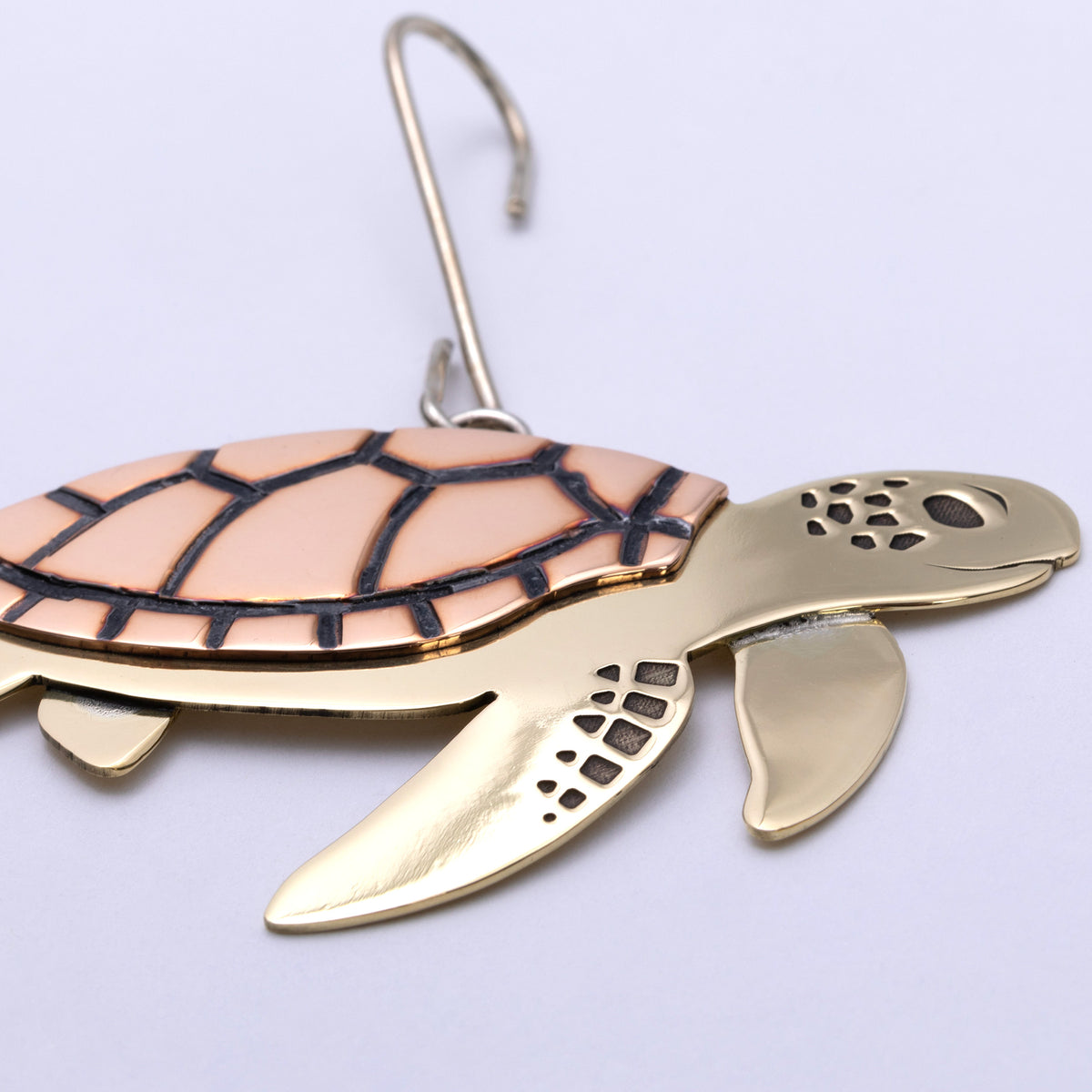 A sea turtle jewelry charm with a gold-plated body and a peach-pink shell outlined in black, attached to a silver metal hook.