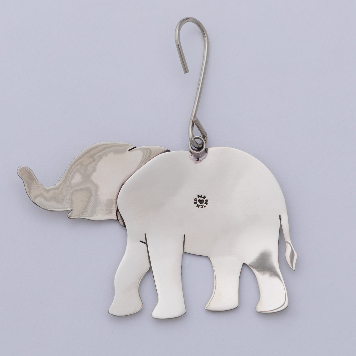 A polished silver elephant-shaped ornament with a curved metal hook at the top, shown against a light lavender background.