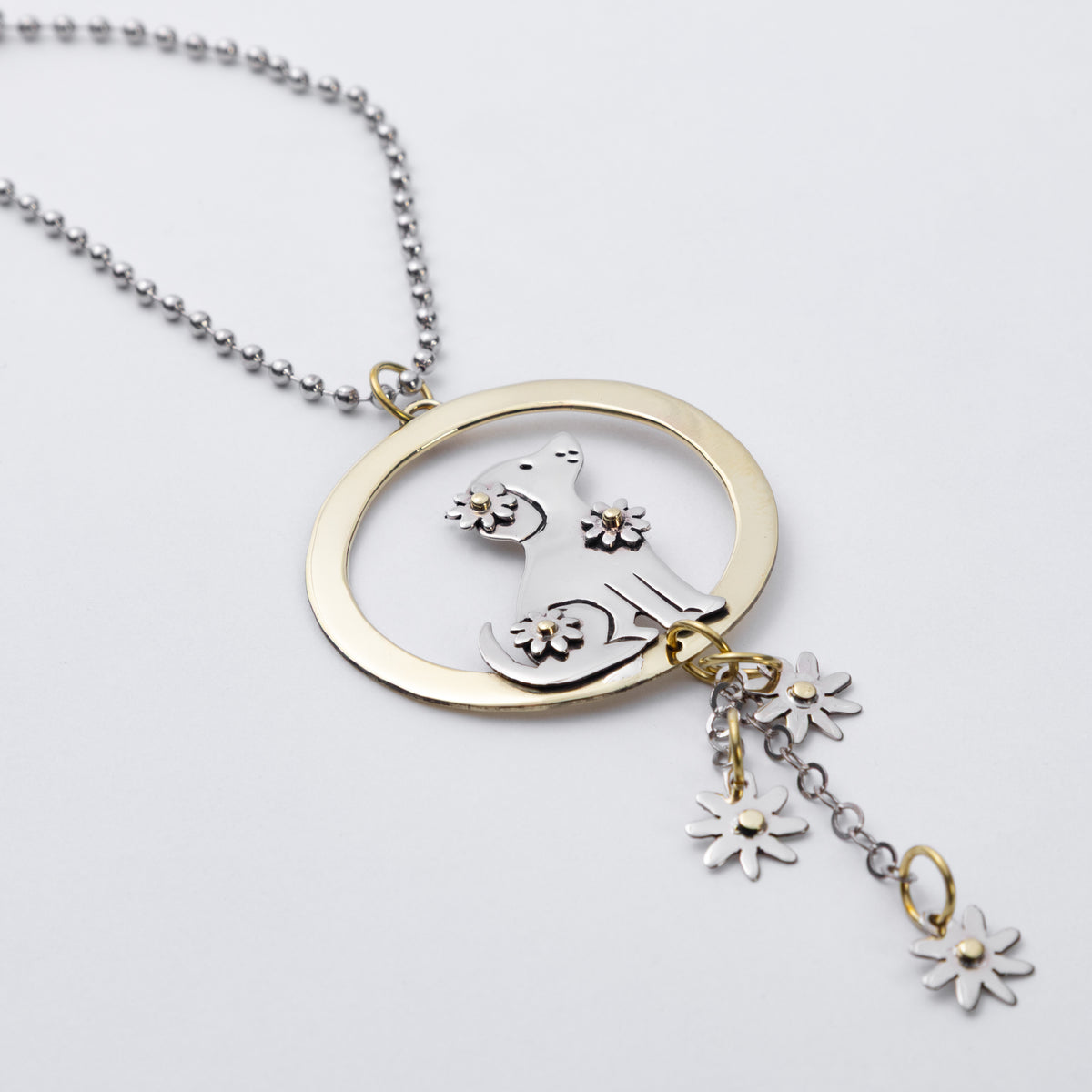 A two-tone silver and brass car charm featuring a circular pendant with a stylized cat silhouette and small flower charms, displayed on a clean white background.