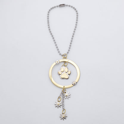 A gold and silver pet memorial necklace featuring a circular pendant with a paw print charm and dangling flower charms, shown on a light gray background.