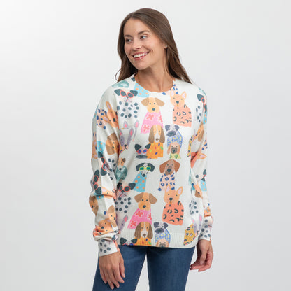 A woman wearing a cream-colored crewneck sweater with a colorful cartoon dog pattern, paired with blue jeans, photographed against a light gray studio background.