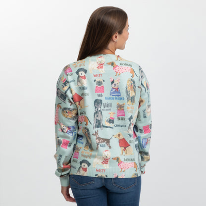 A woman viewed from the back wearing a light blue-green crewneck sweater with a colorful dog-themed graphic print, paired with blue jeans against a plain white background.