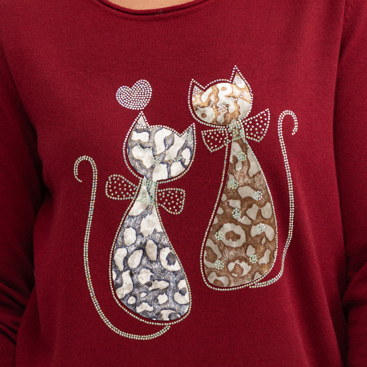 A close-up of a burgundy long-sleeve top featuring a decorative graphic of two stylized cats with leopard and cheetah-style spots, outlined with rhinestones, on the chest.