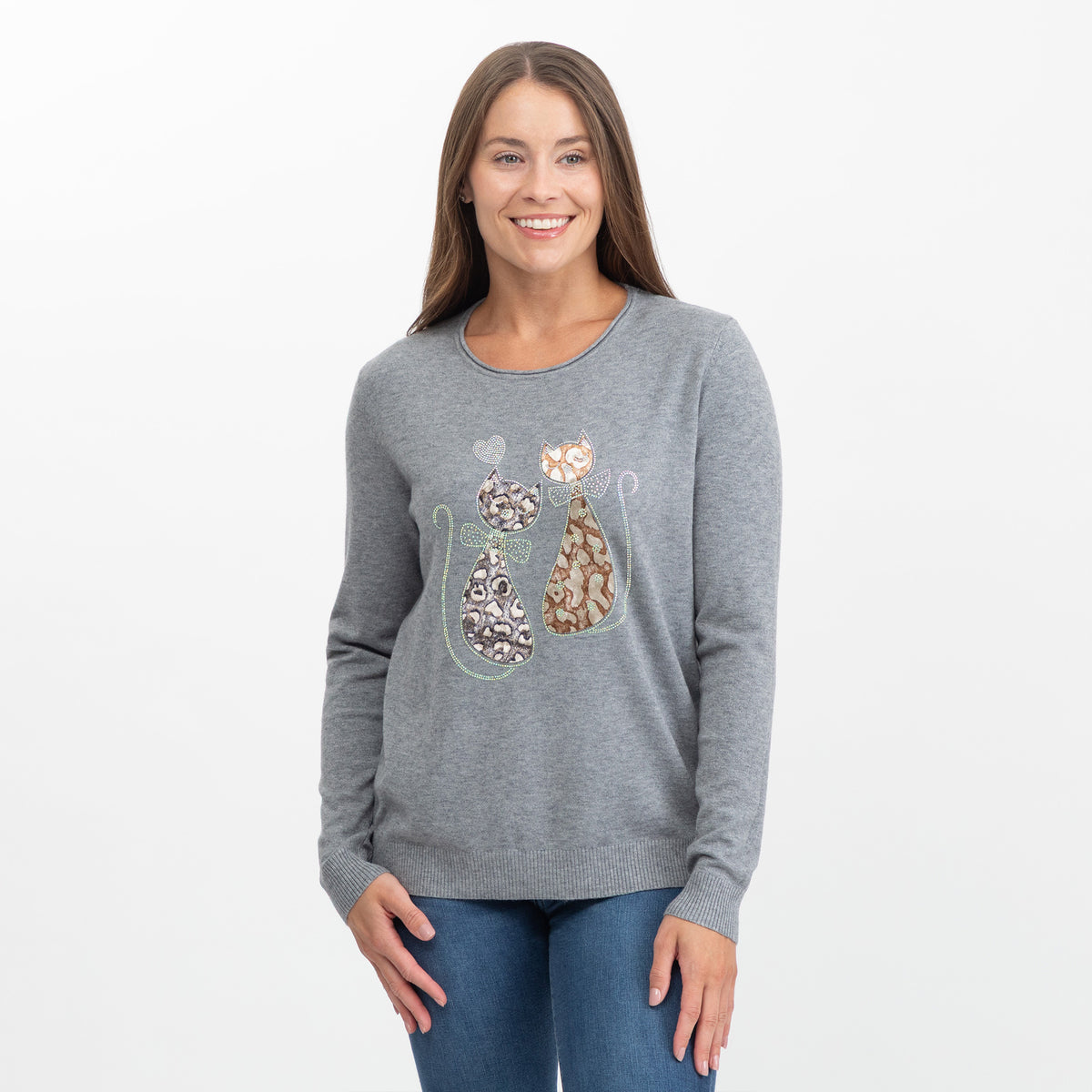 A woman modeling a heather gray long-sleeve crewneck sweater with a graphic of two cats on the front, paired with blue jeans against a plain white studio background.