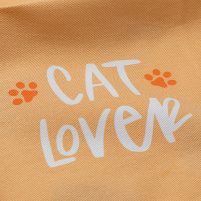 A close-up of a peach-colored fabric with a printed design that reads 'CAT LOVER' in white script, accented by two orange paw prints.