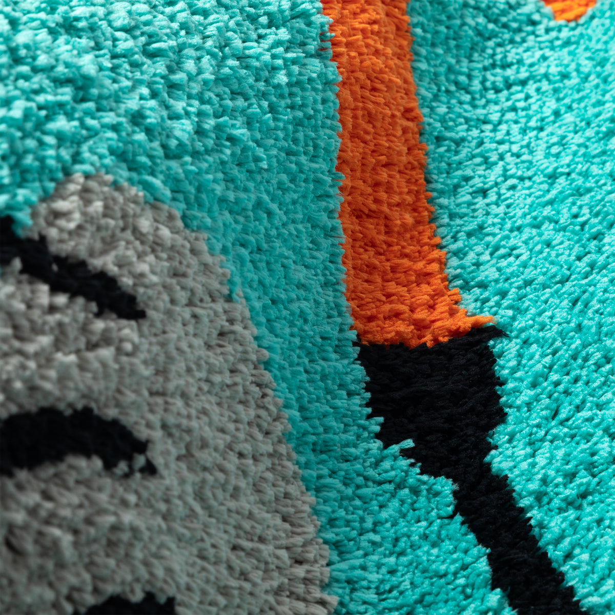 Close-up of a high-pile shag rug with a bold abstract pattern in turquoise, orange, black, and light gray.