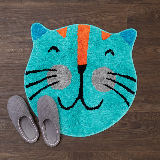 A turquoise cat-face shaped rug with an orange stripe, black whiskers and nose, and gray cheeks, styled on a dark wood floor with a pair of gray slip-on shoes beside it.