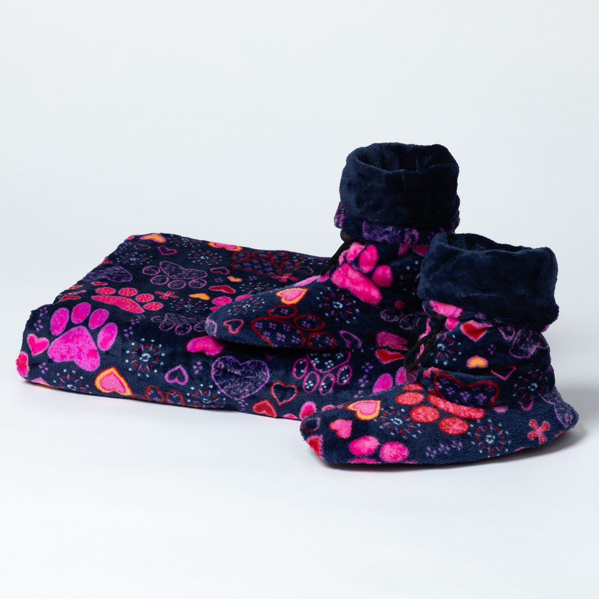 A plush pet blanket and matching booties in a dark navy blue fleece fabric with a colorful pattern of pink paw prints, hearts, and butterflies, set against a plain white studio background.